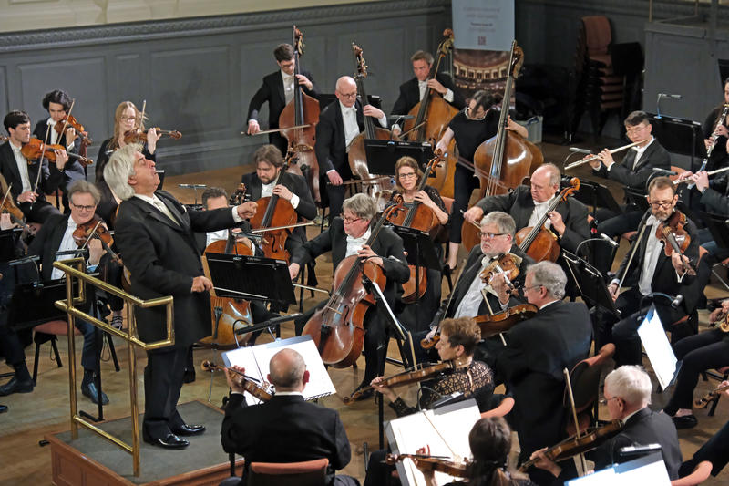 The conductor of the Oxford Philharmonic Orchestra directing the musicians at the front and centre of the auditorium