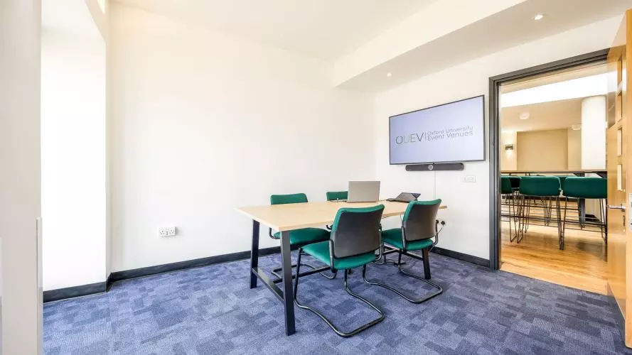 Meeting room with rectangular table and four green chairs placed on the outside