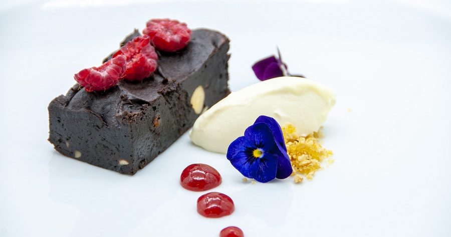 This image shows a chocolate brownie with raspberries and a fruit couli